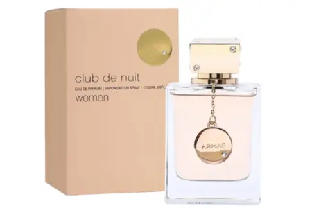 Armaf Club de Nuit Mujer 8 Club de Nuit Mujer: Frasco cuadrado de vidrio transparente con placa colgante dorada y caja rosa clara con detalles metálicos.